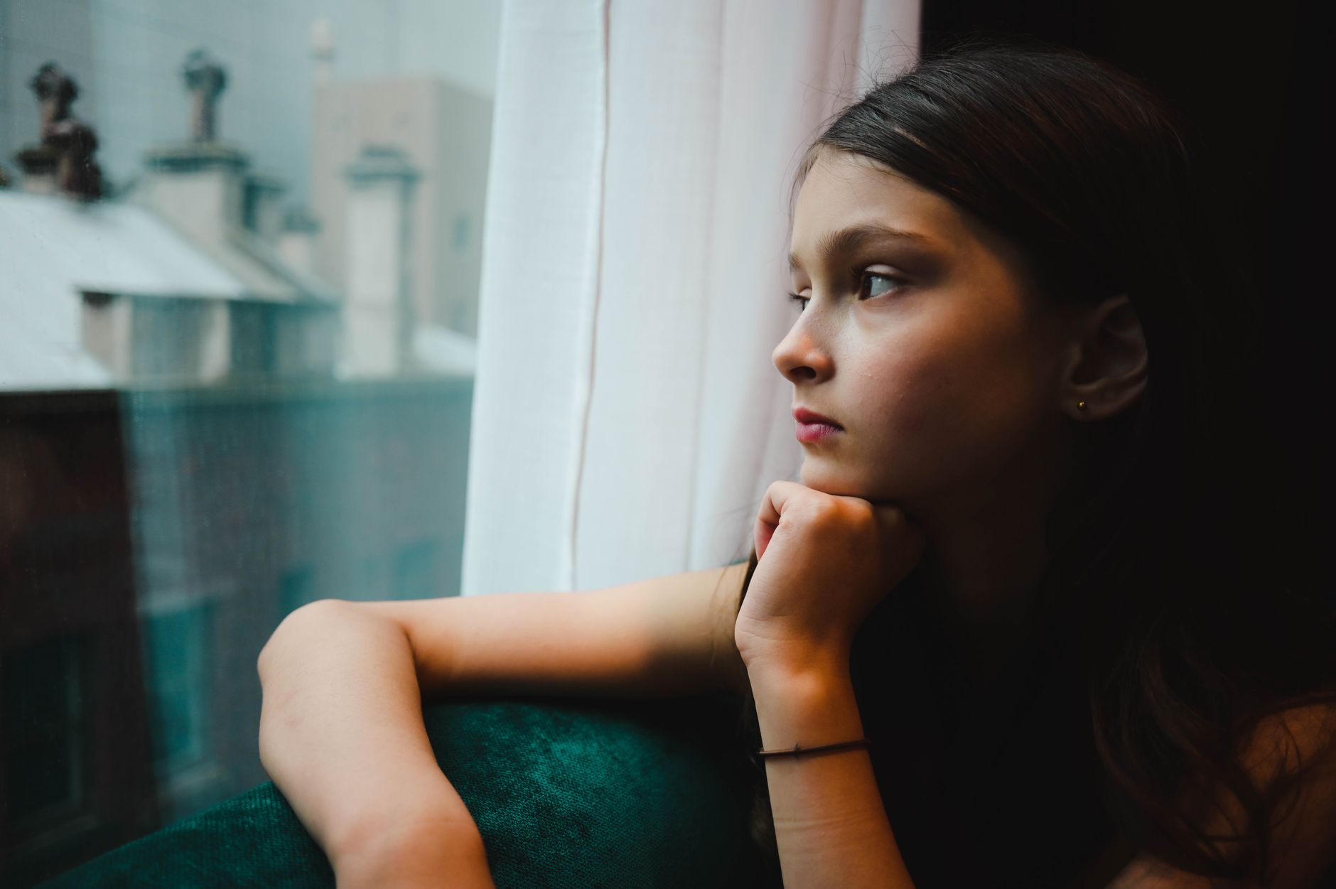 Adolescente pensive regardant par la fenêtre, le menton posé sur la main